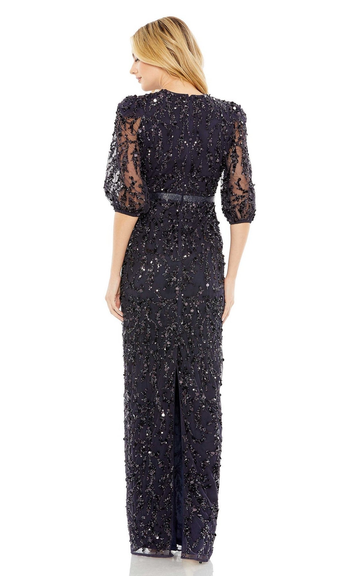 A woman faces away, wearing the Mac Duggal 93790 Long Sleeve Beaded Formal Dress with sheer sleeves and a back slit, standing against a plain white background.